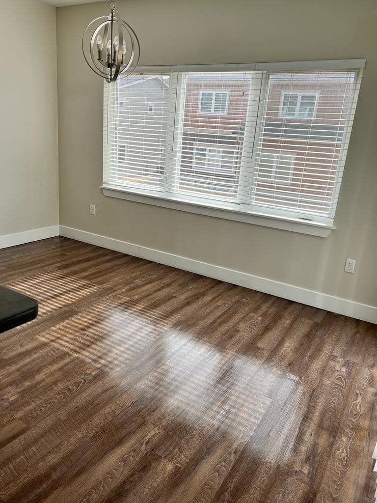 Empty room with wood-look flooring, a window with blinds, and a light fixture.