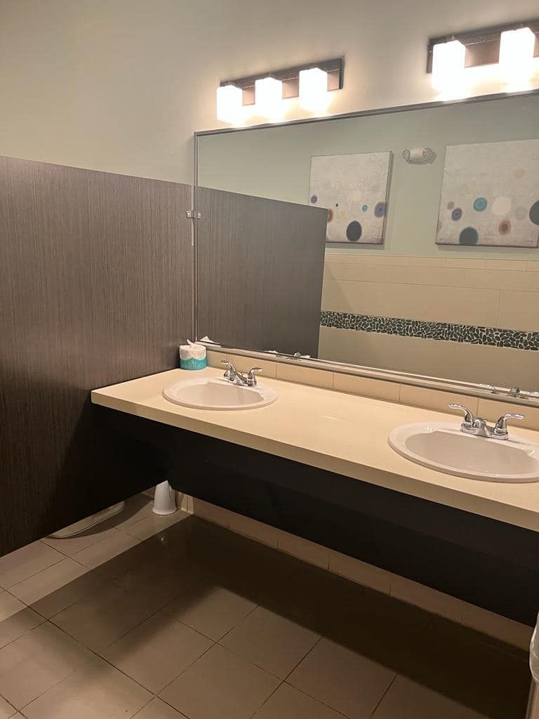 Public restroom with two sinks, a large mirror, and stall dividers.