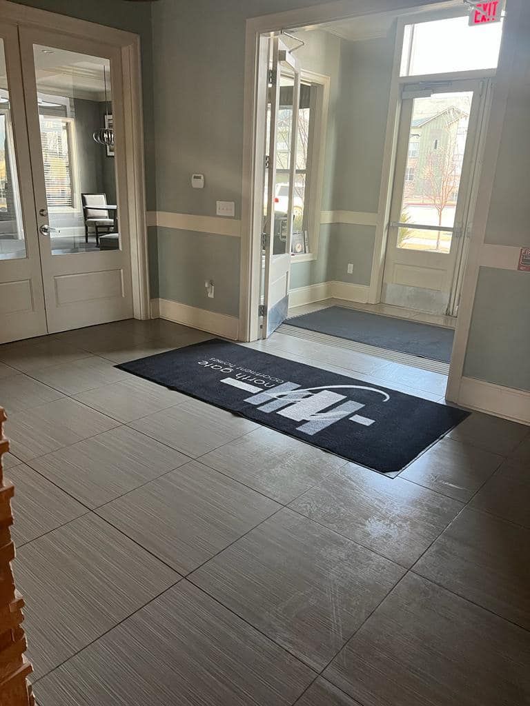 Entryway with gray floor tiles, open doors, and a welcome mat. Light blue walls and white trim.
