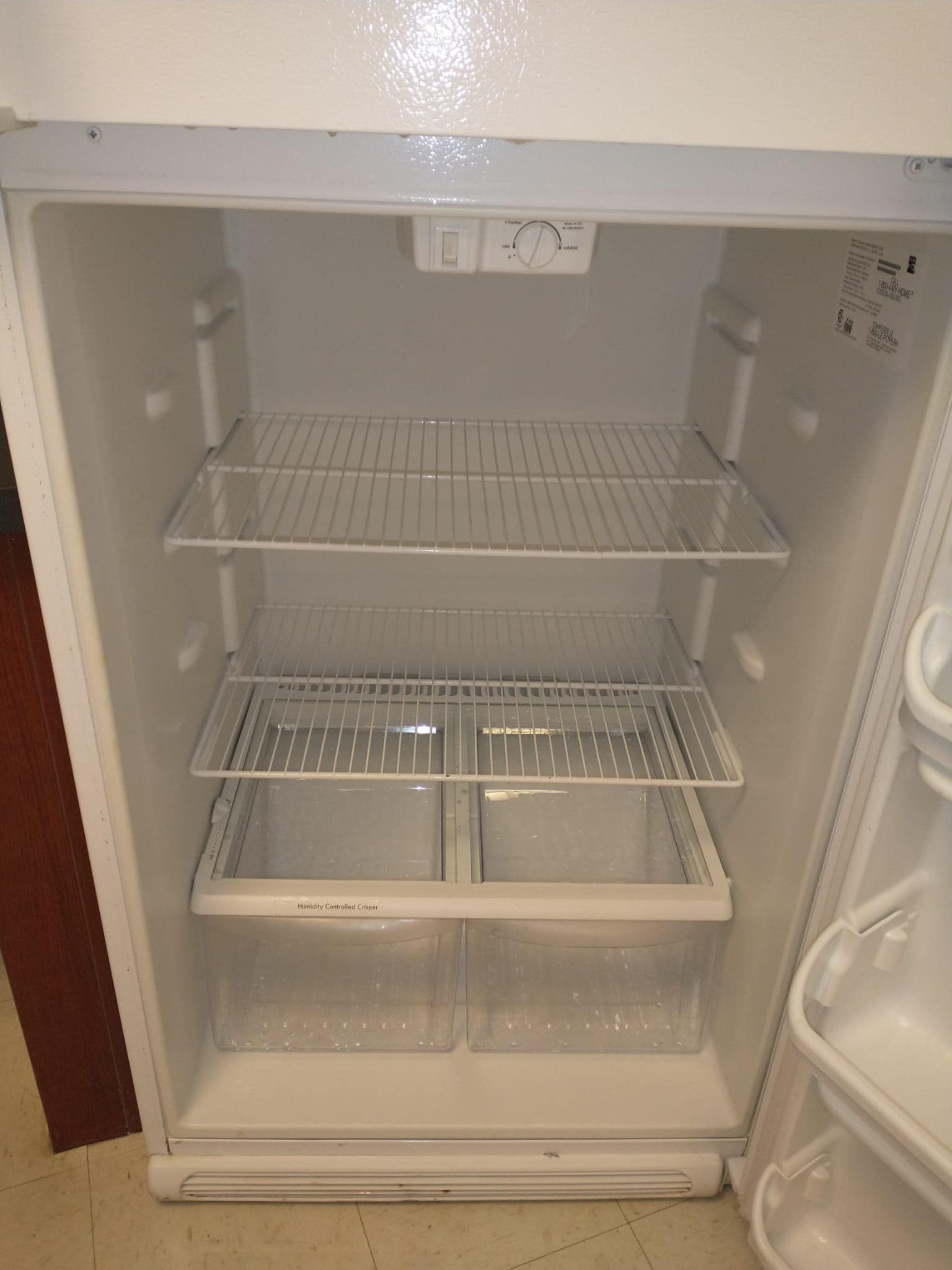 Empty white refrigerator with wire shelves and clear drawers.