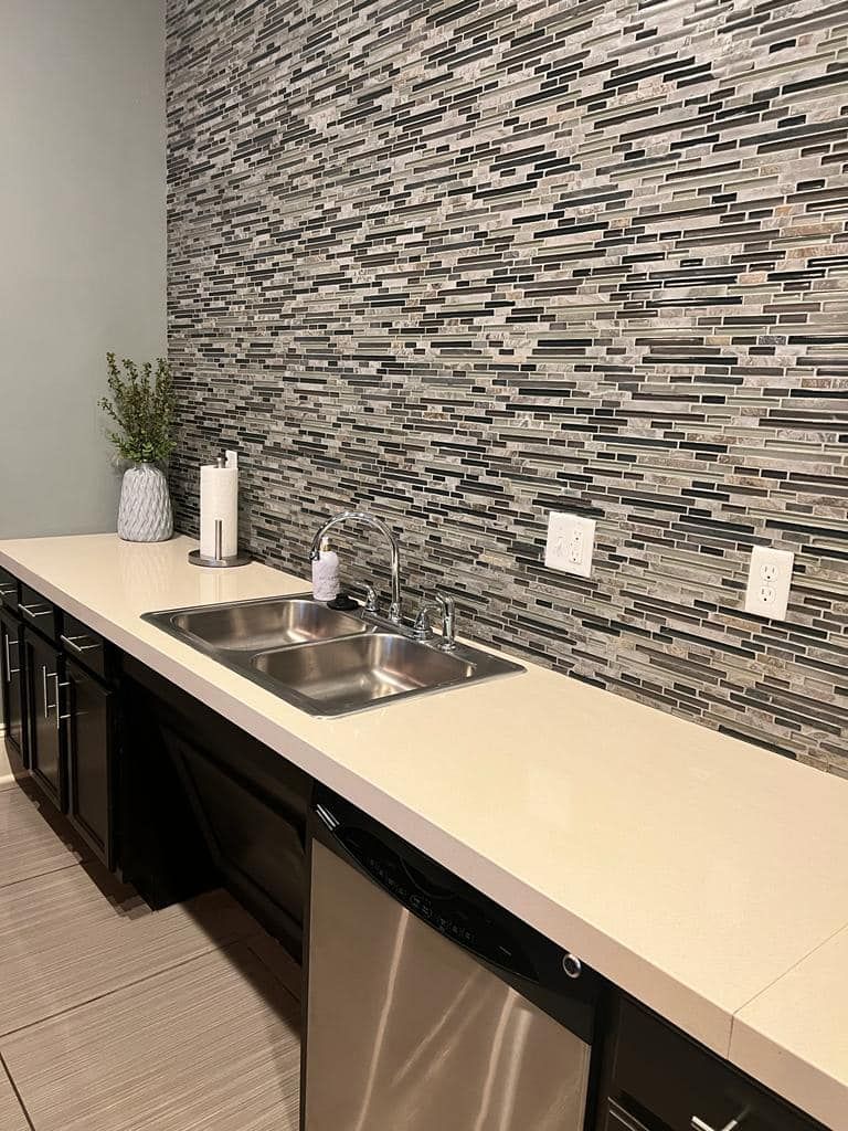Kitchenette with a sink, dishwasher, and tile backsplash. Black cabinets and white countertop.