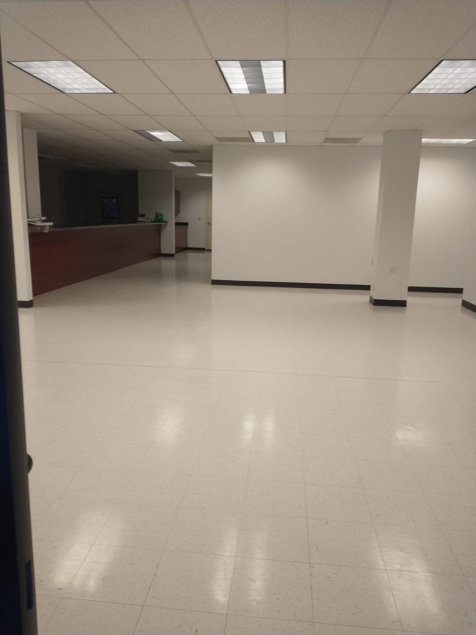 Empty, bright white office space; polished white floor, white walls, overhead lighting, brown counter.