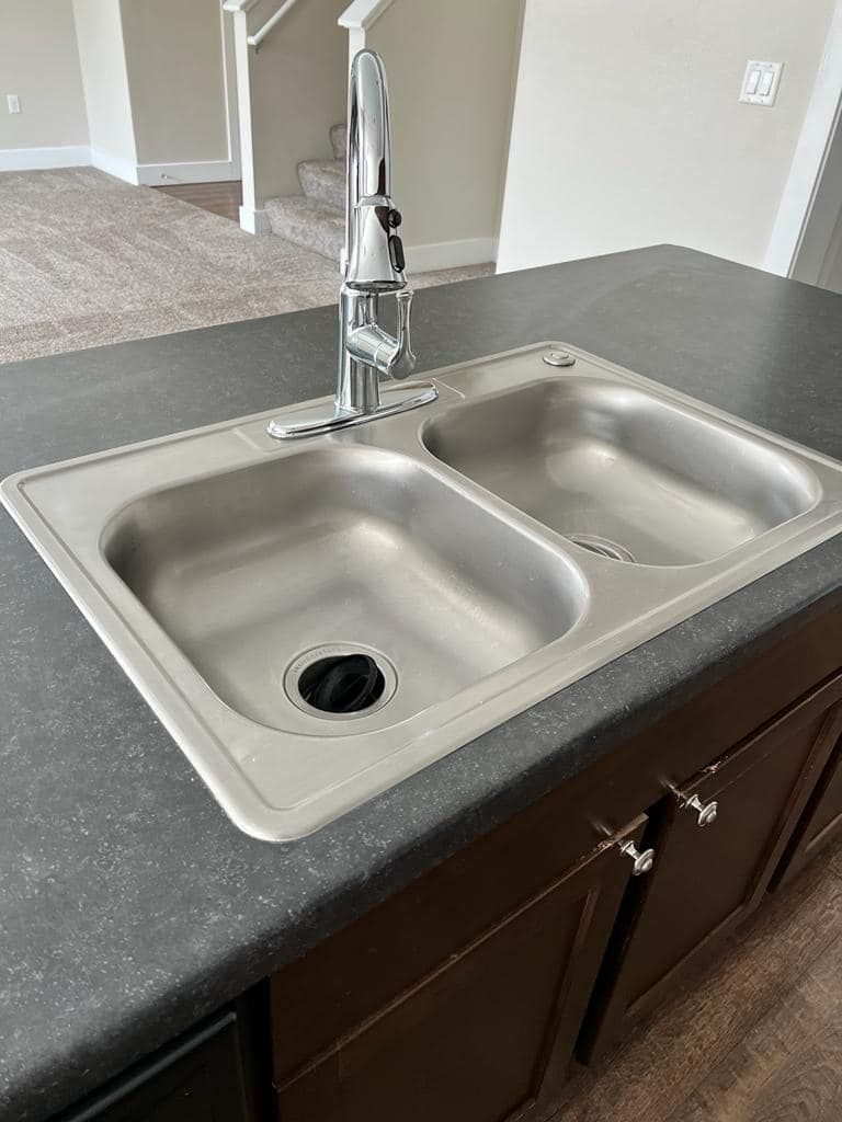 Stainless steel double sink in a kitchen countertop, with a chrome faucet.