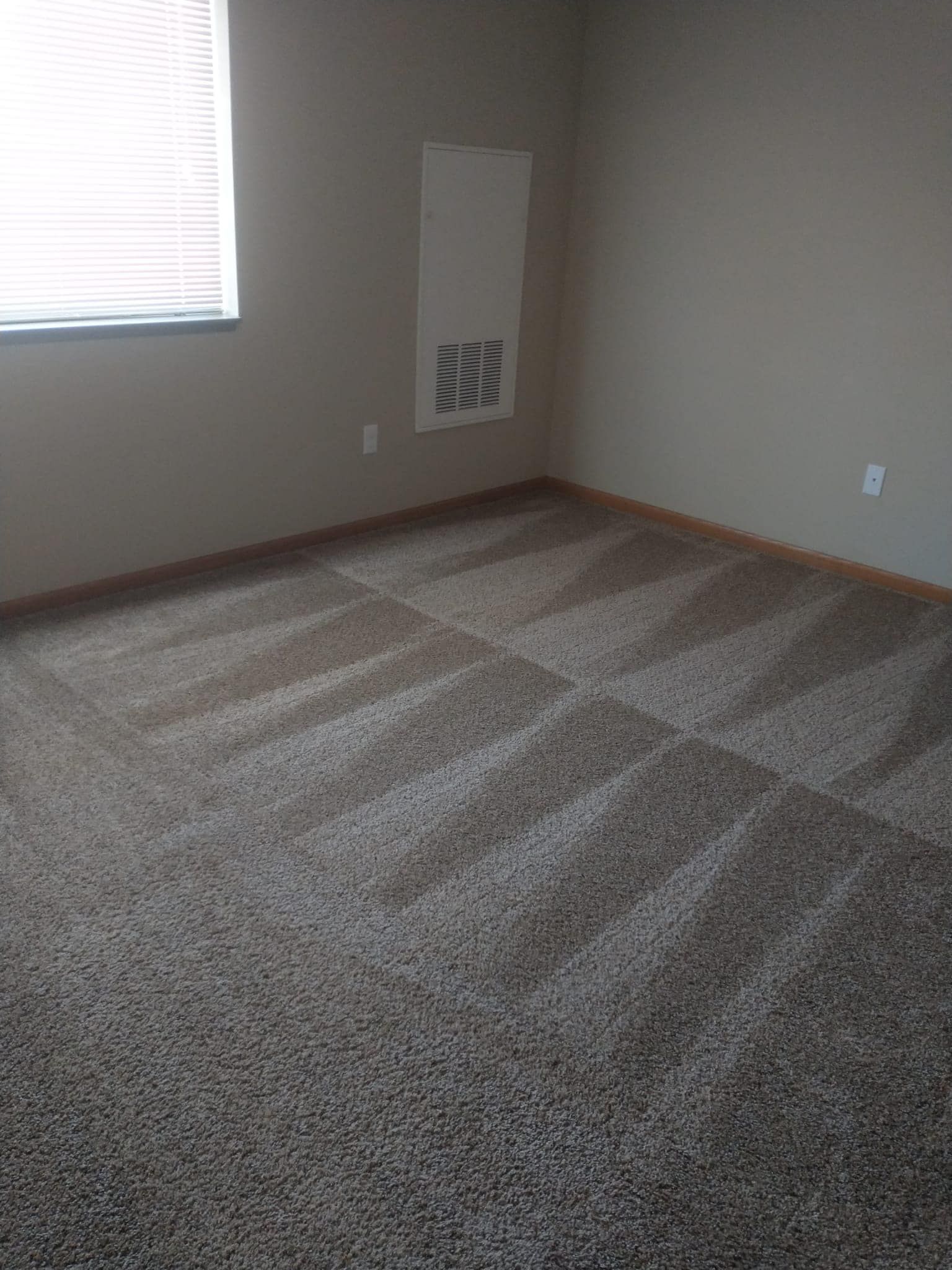 Empty room with patterned carpet, window, and wall vent.
