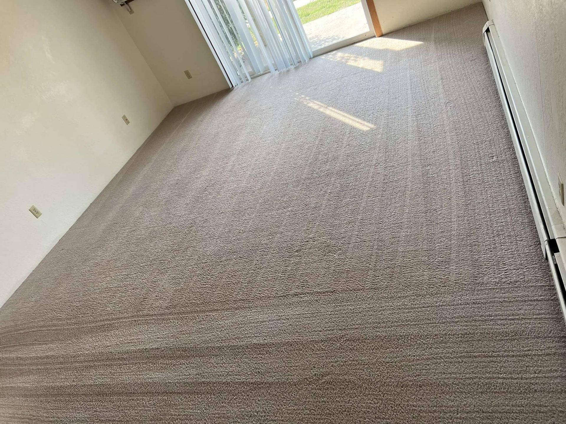 Room with light brown carpet, sliding glass door, and white walls. Sunlight streams in.