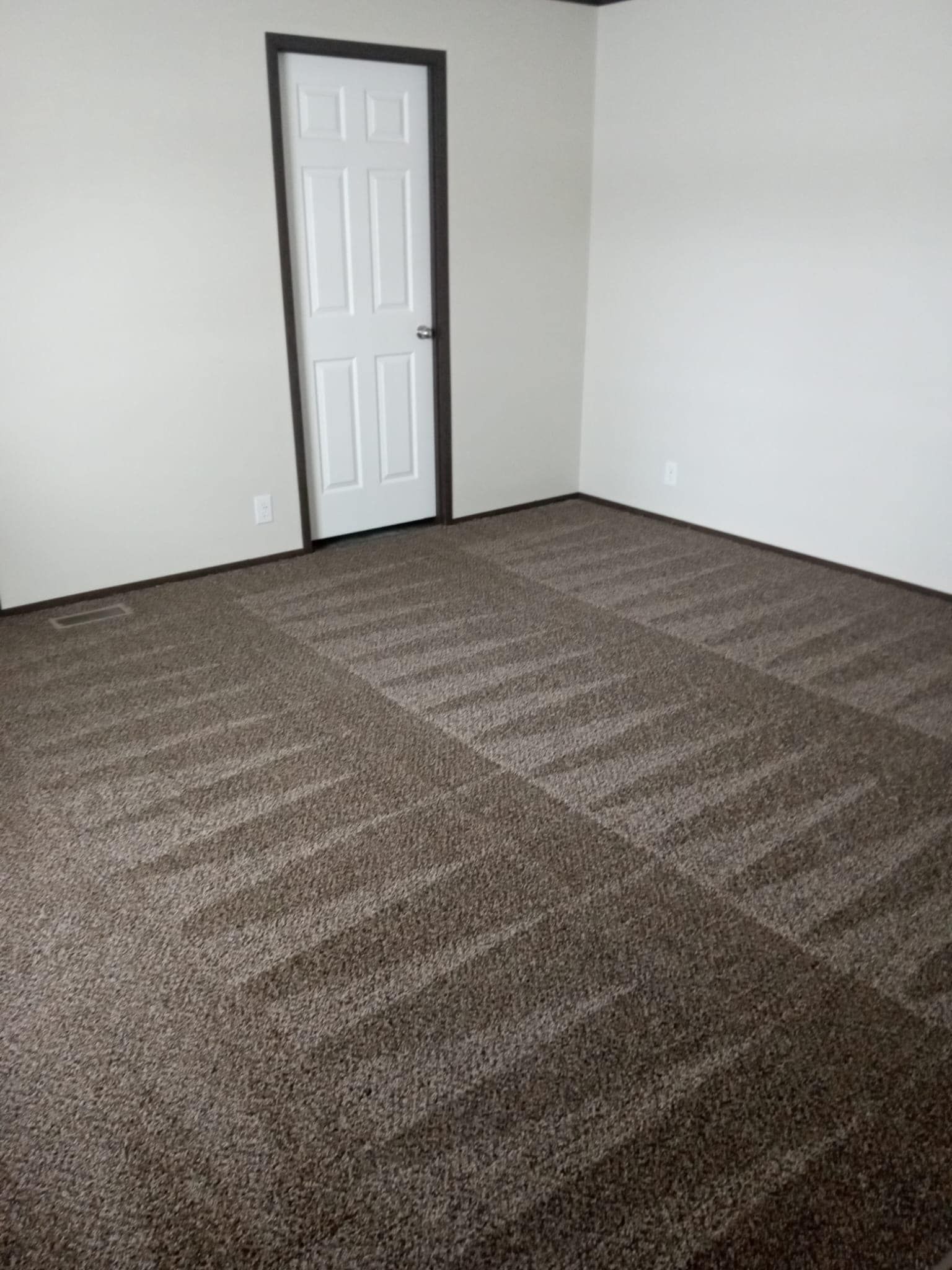 Empty room with brown carpet in a square pattern, beige walls, and a white door with dark trim.