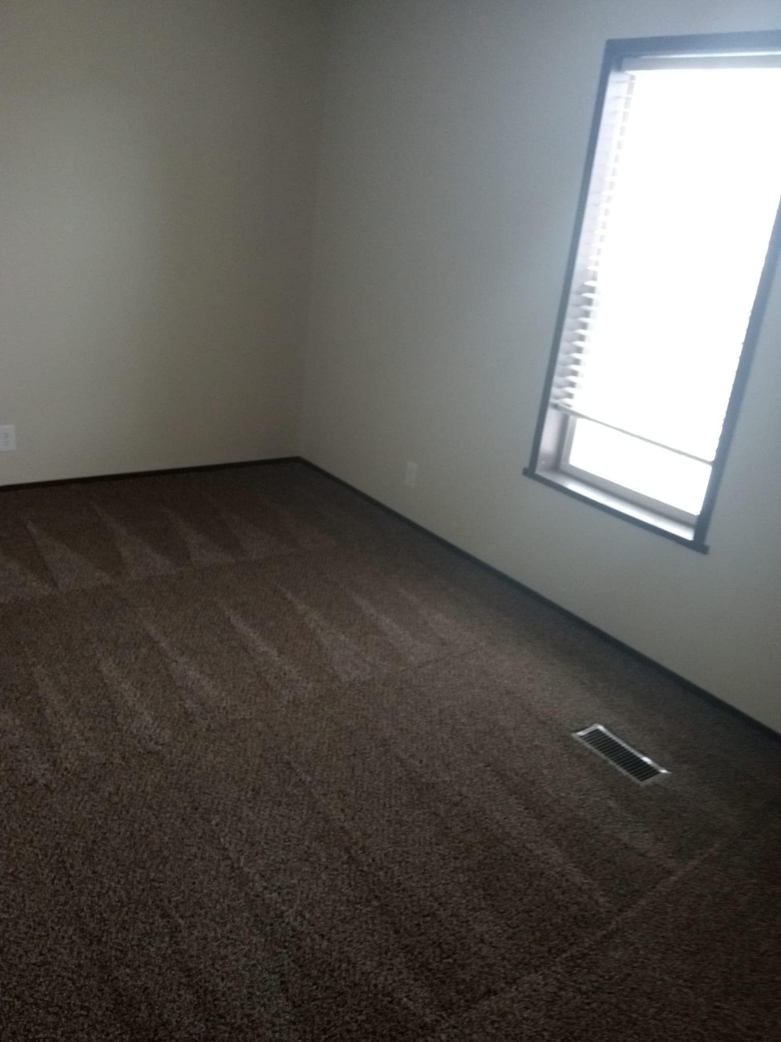 Empty room with brown carpet, tan walls, and a window with blinds.