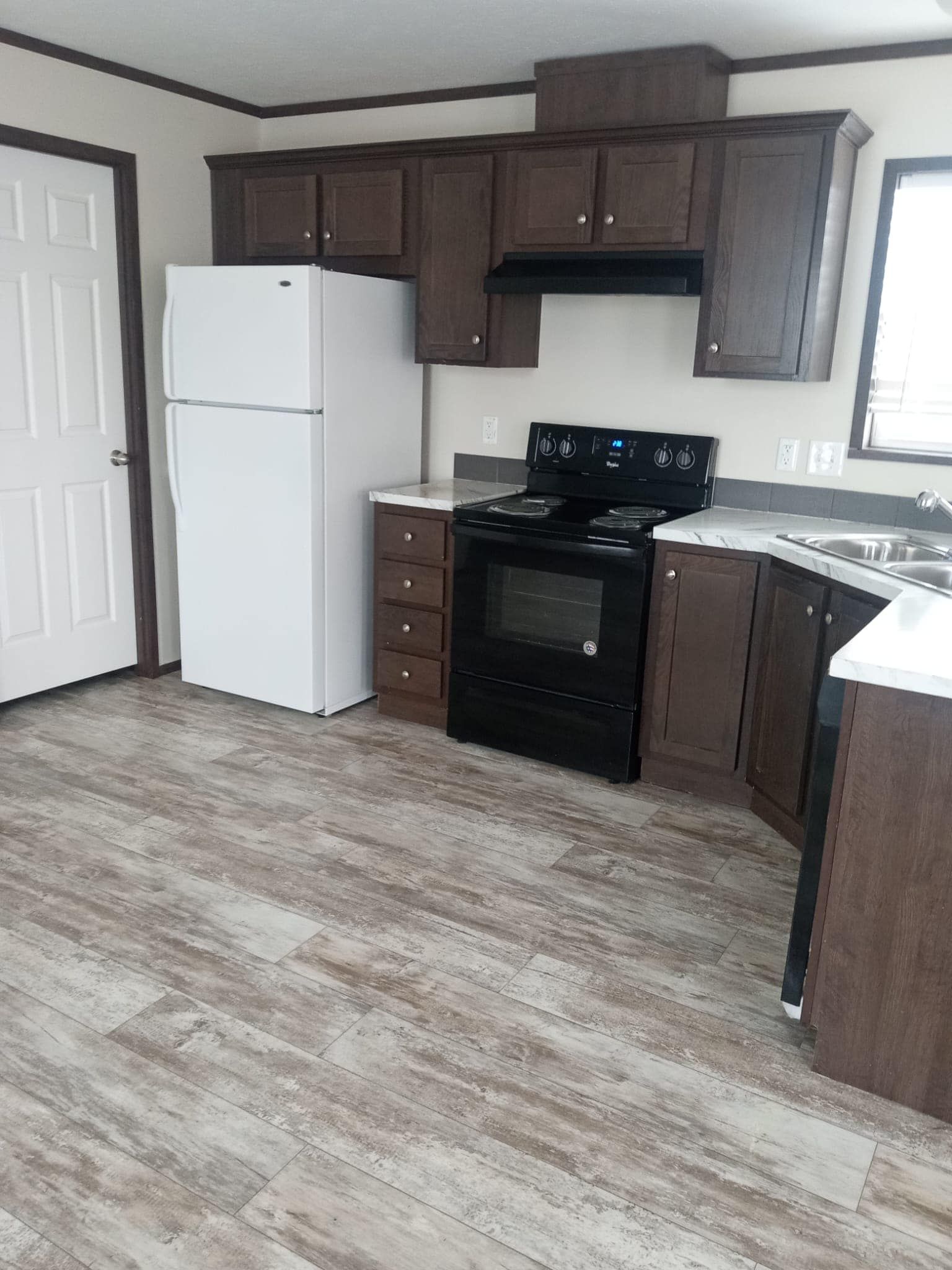 Kitchen with brown cabinets, white refrigerator, black stove, and light wood-look flooring.