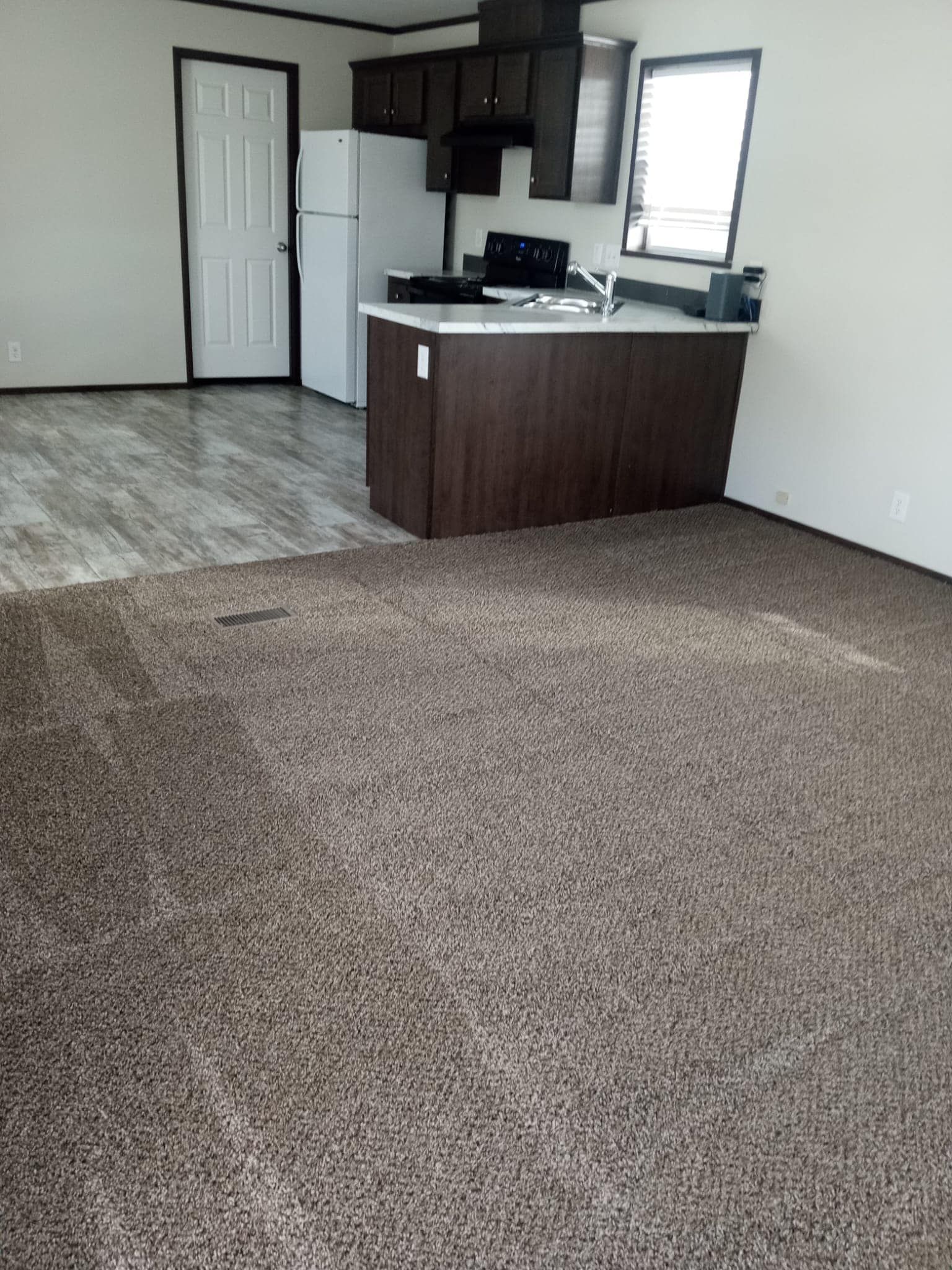 Open-concept living space with dark brown island, kitchen with white appliances, and carpeted floors.