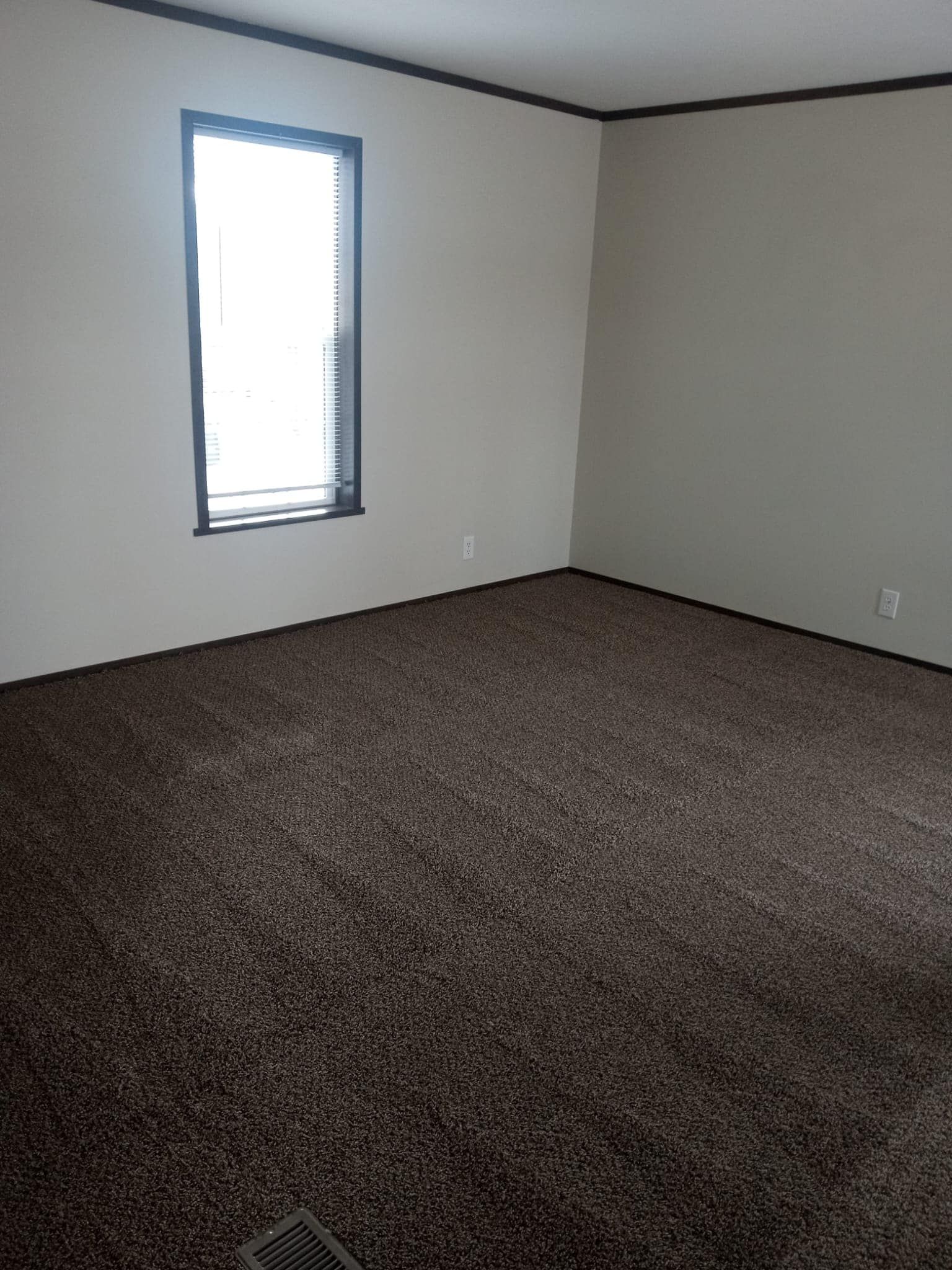 Empty room with dark brown carpet, white walls, and a window.