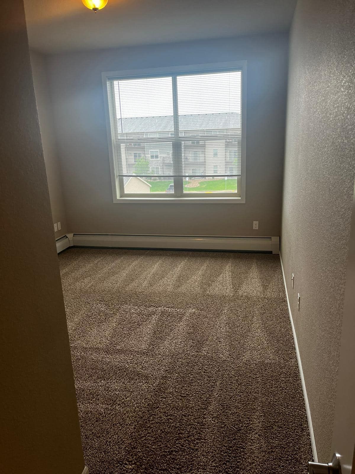 Empty room with beige walls, brown carpet, and a window with blinds.