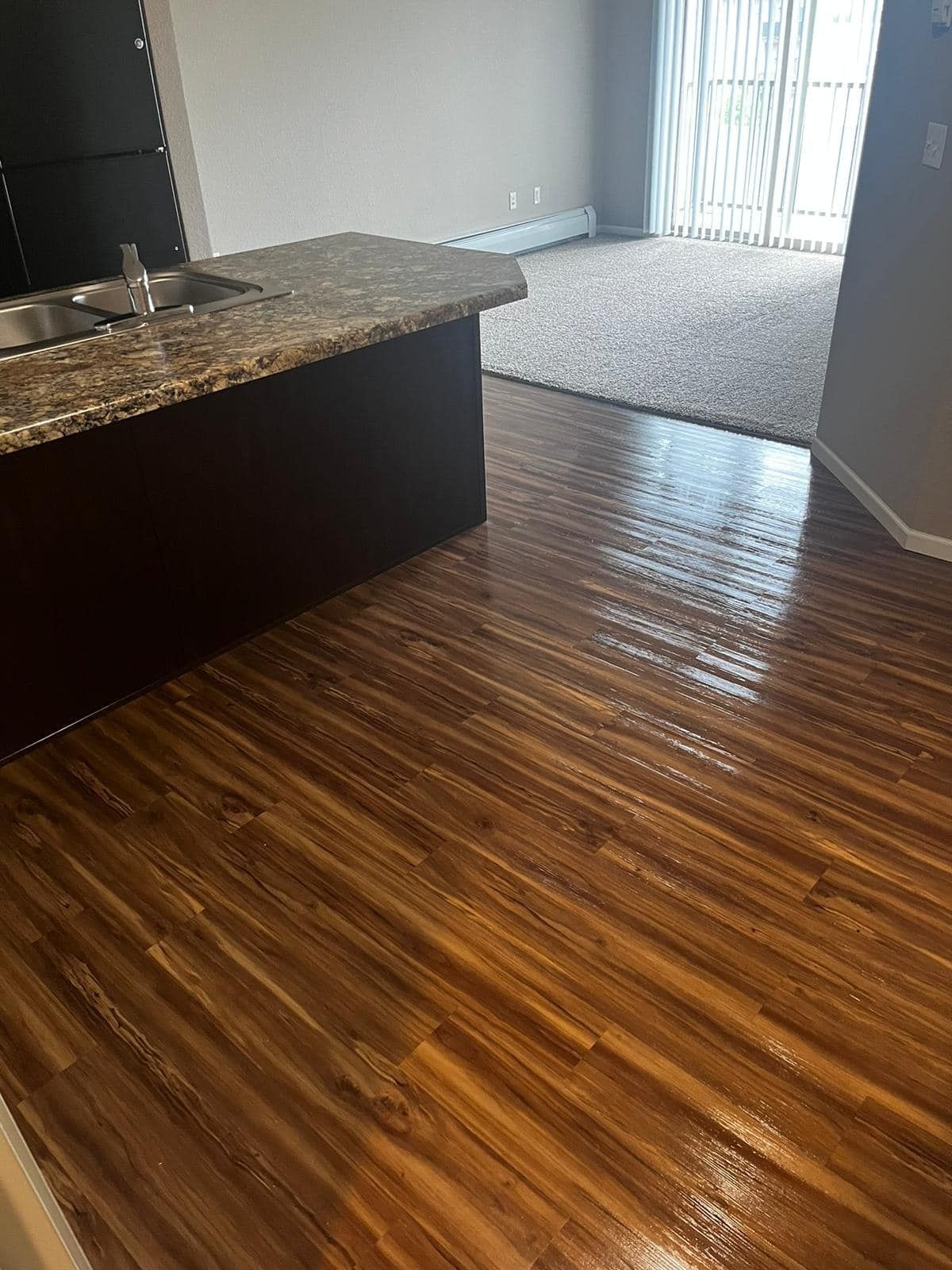 Wooden floor in a room, with a kitchen island and a carpeted living area visible.