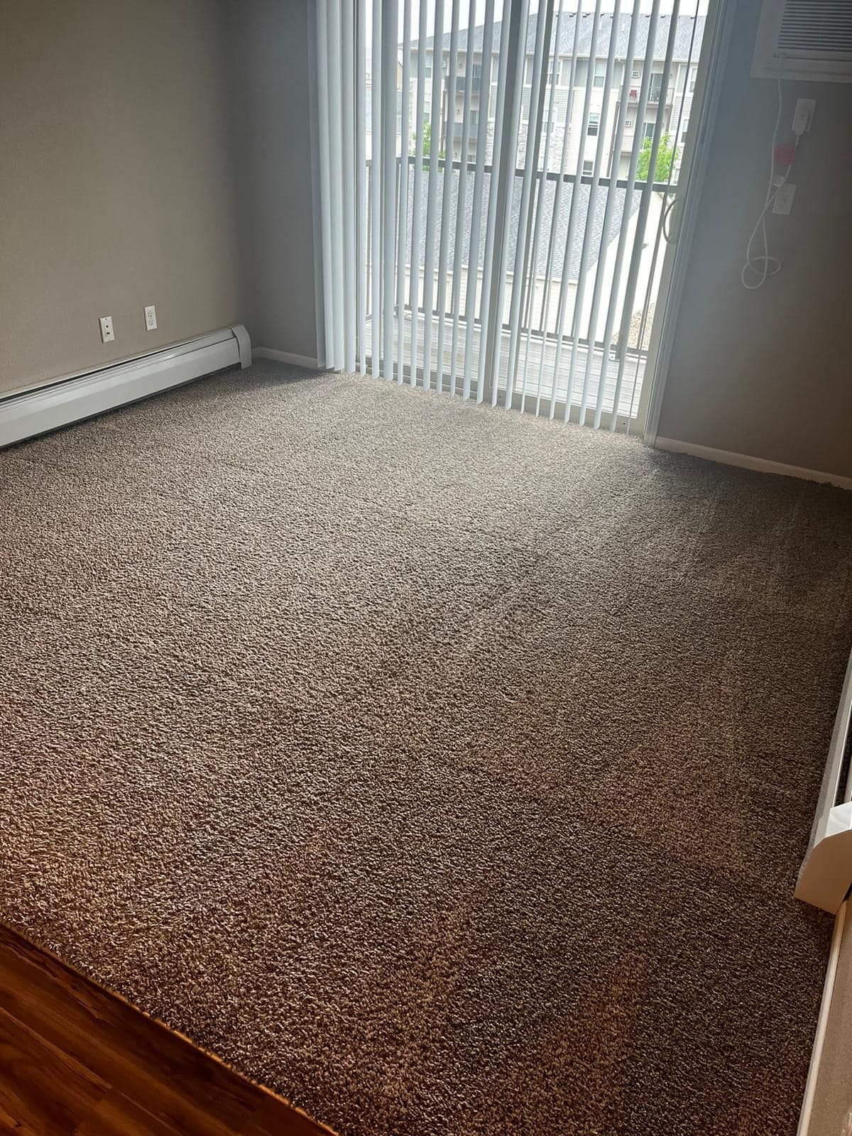 Empty room with beige carpet, sliding glass door, and neutral walls.