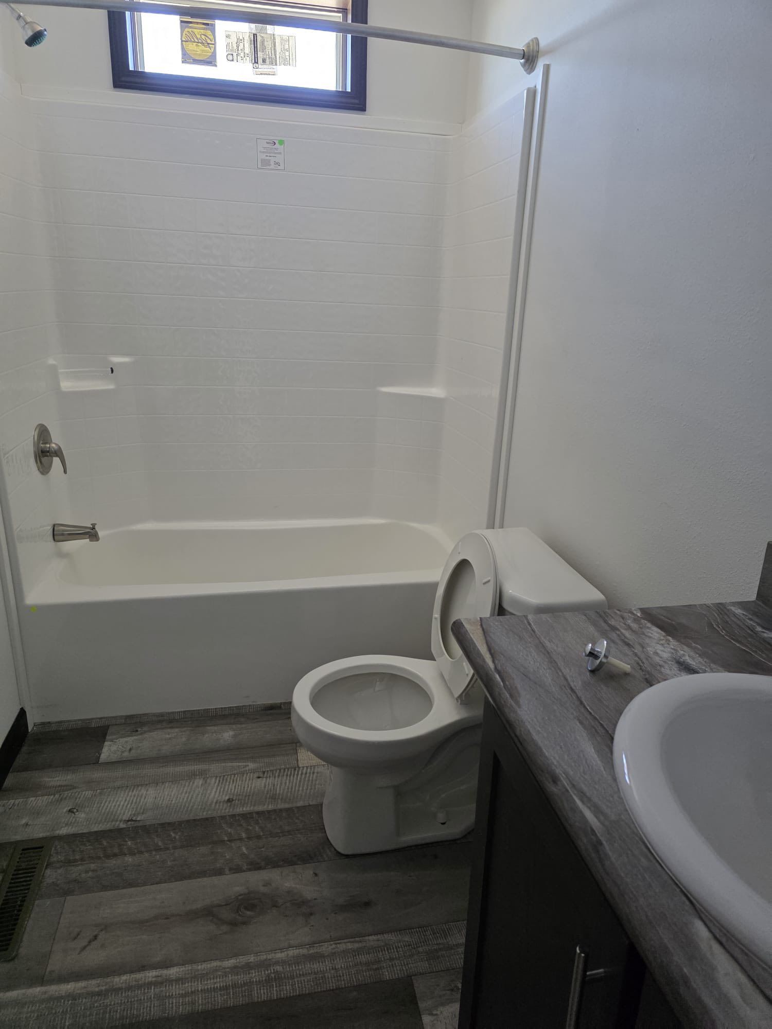Bathroom with white fixtures: toilet, sink, bathtub/shower combo. Gray wood-look flooring.