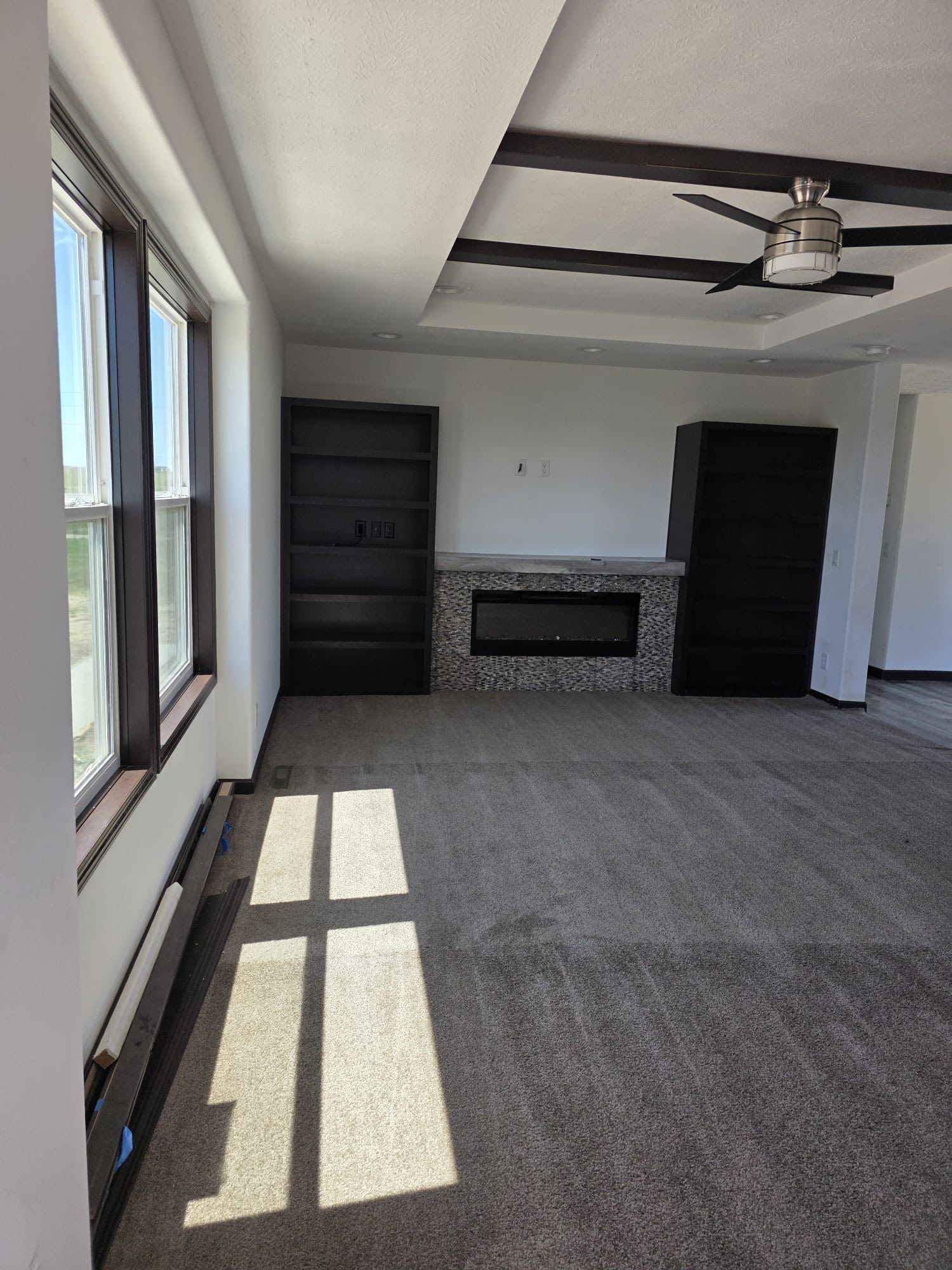 Living room with fireplace, built-in bookshelves, ceiling beams, and a window with natural light.