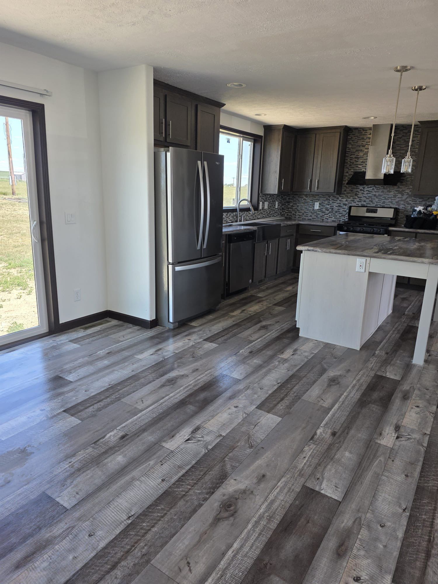 Modern kitchen with gray cabinets, stainless steel appliances, and wood-look flooring.