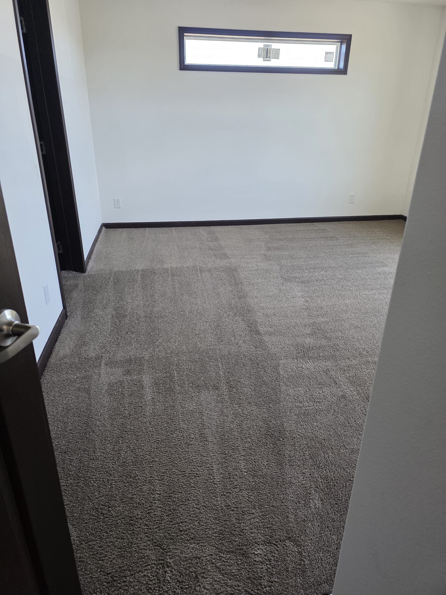 Empty room with dark brown trim, tan carpet, and a small rectangular window.