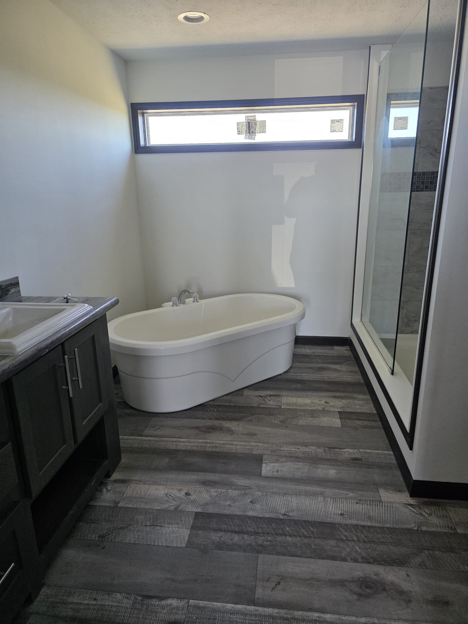 Bathroom with a freestanding tub, dark cabinets, and a glass shower. Gray wood-look flooring.