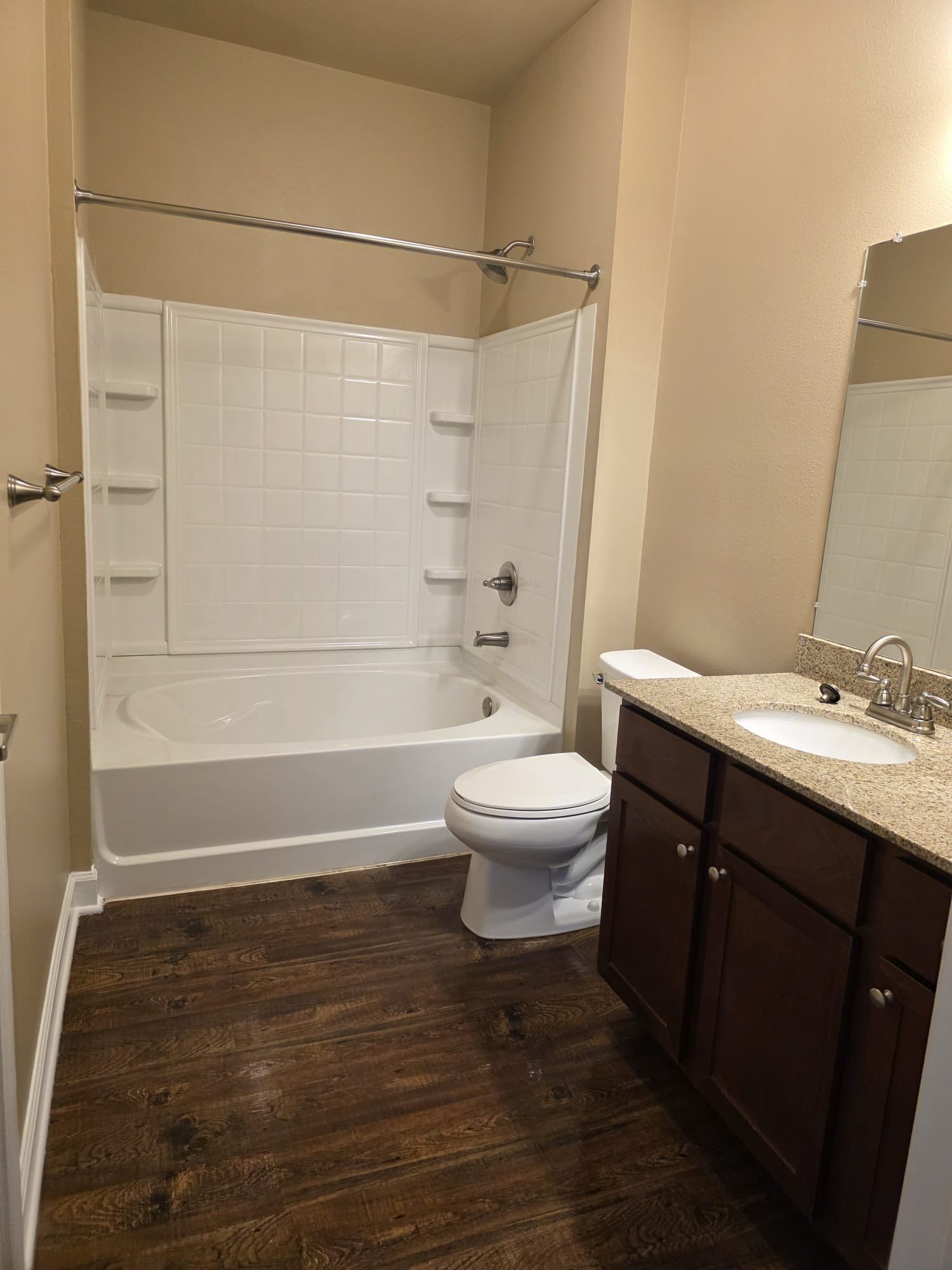 Bathroom with white tub/shower, toilet, dark brown vanity, and wood-look floor.