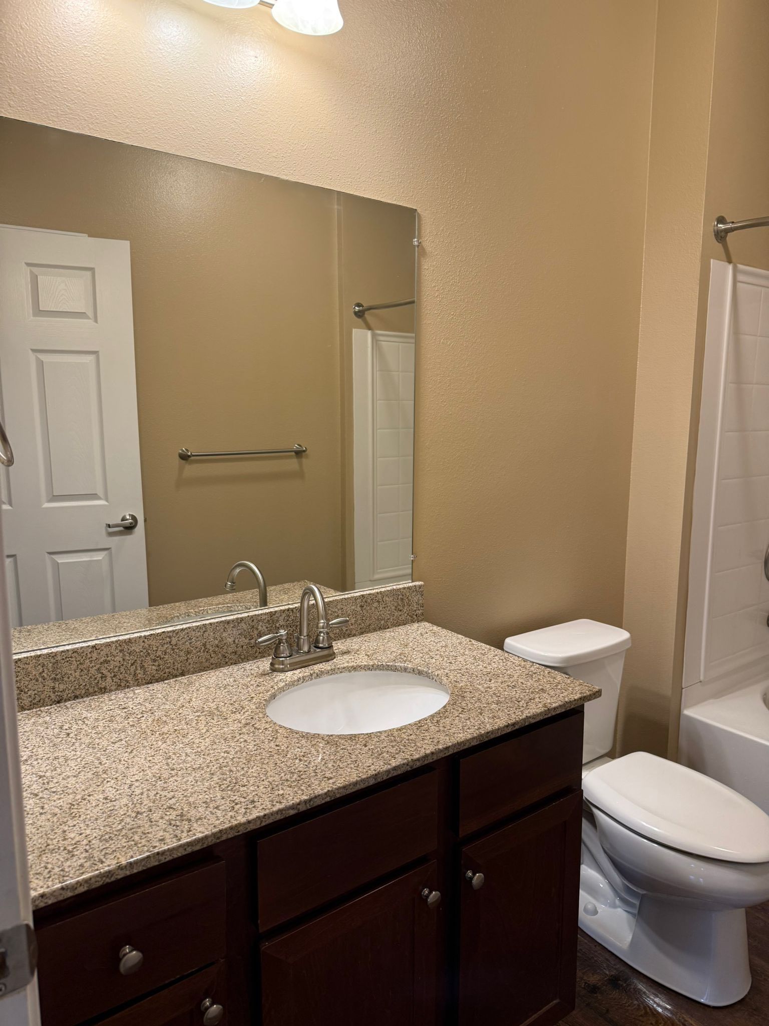 Bathroom with brown cabinets, granite countertop, large mirror, and white toilet.
