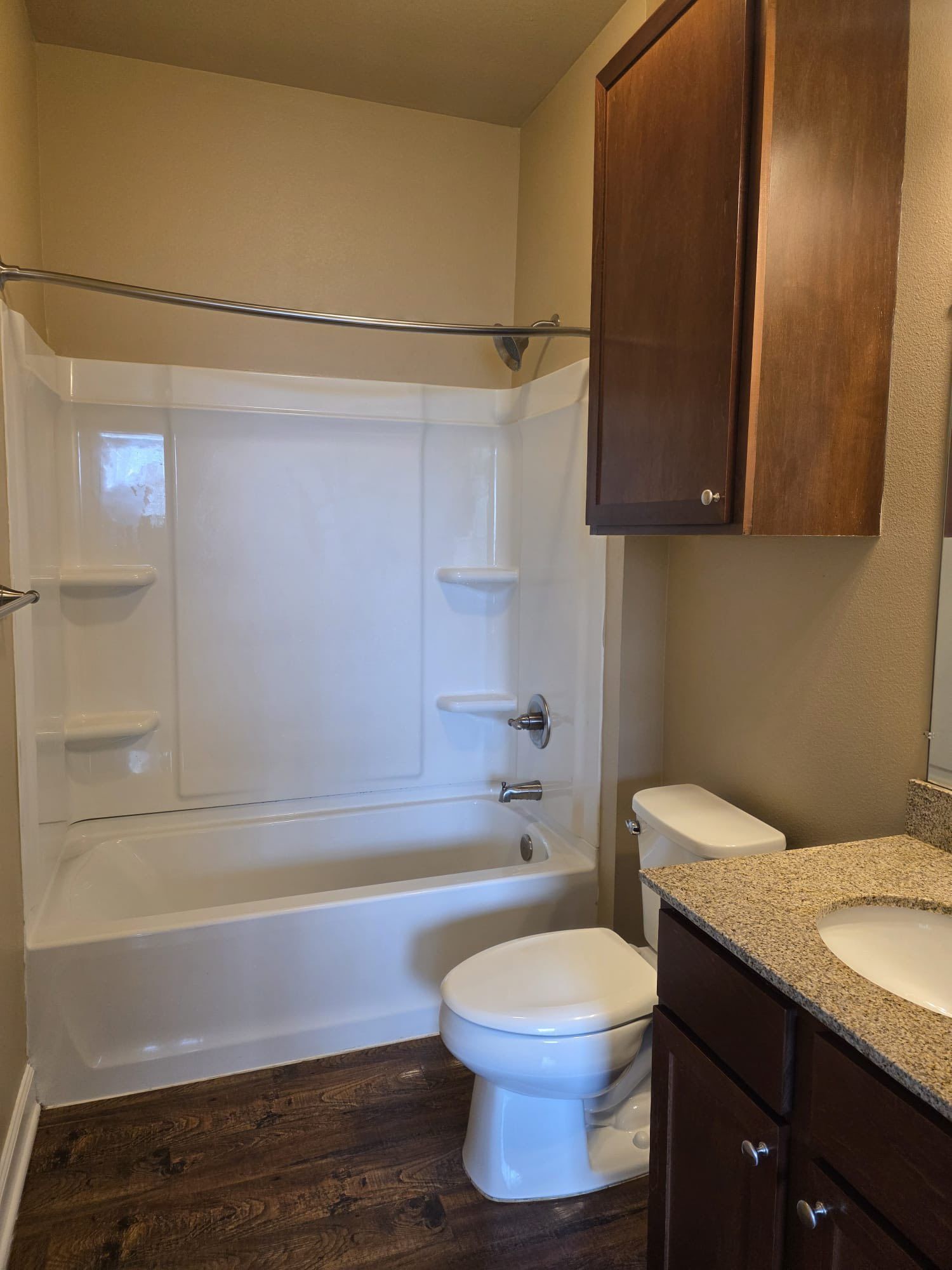 Bathroom with white tub/shower, toilet, dark brown vanity, and wood-look flooring.