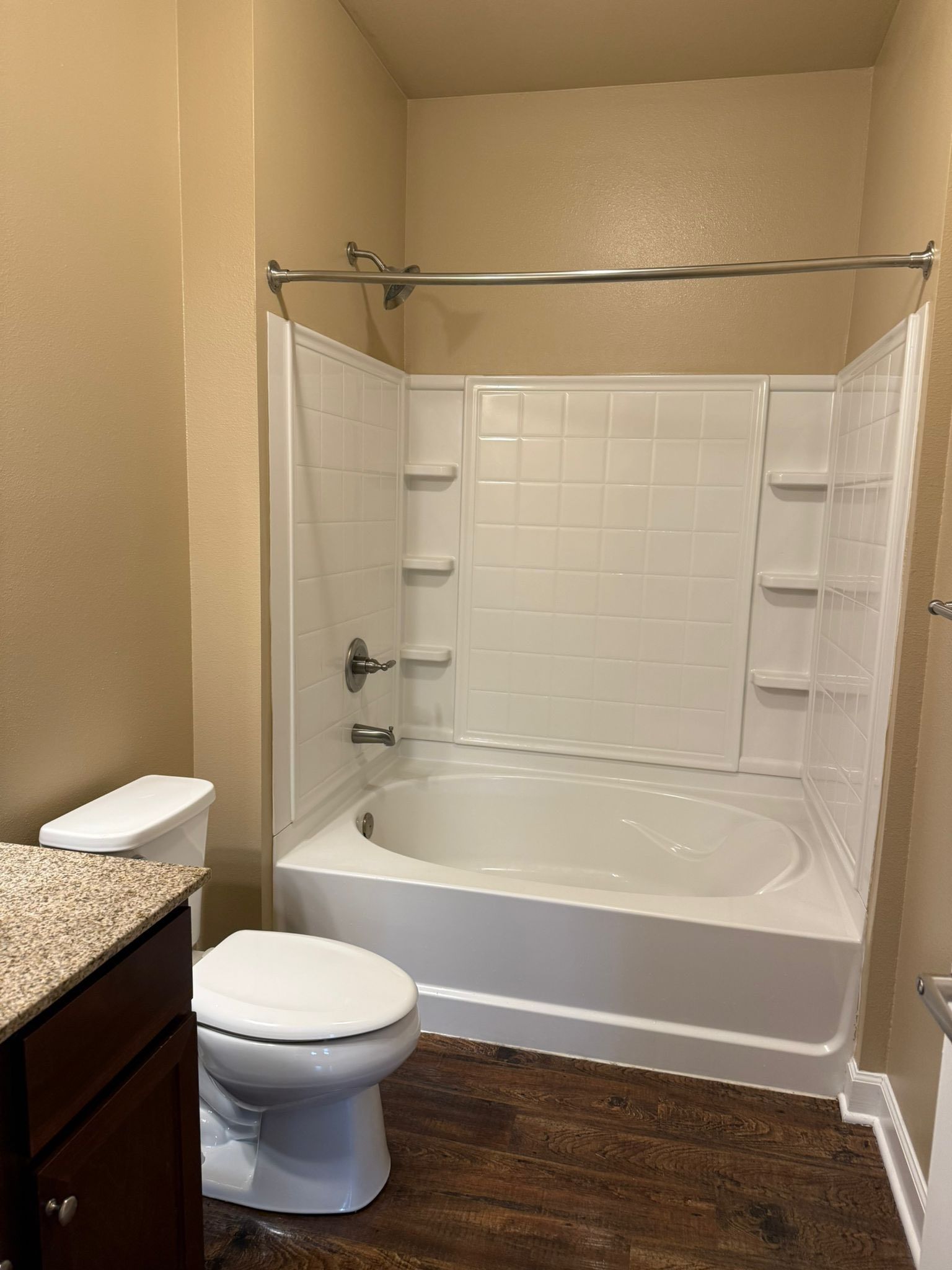 Bathroom with white tub/shower combo, toilet, dark cabinets, and brown flooring.