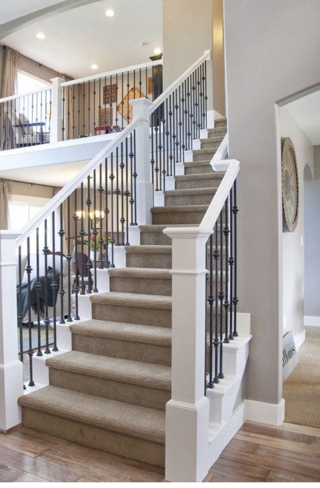 Staircase with carpeted steps, white banisters, and black metal spindles. Second-floor railing visible in the background.