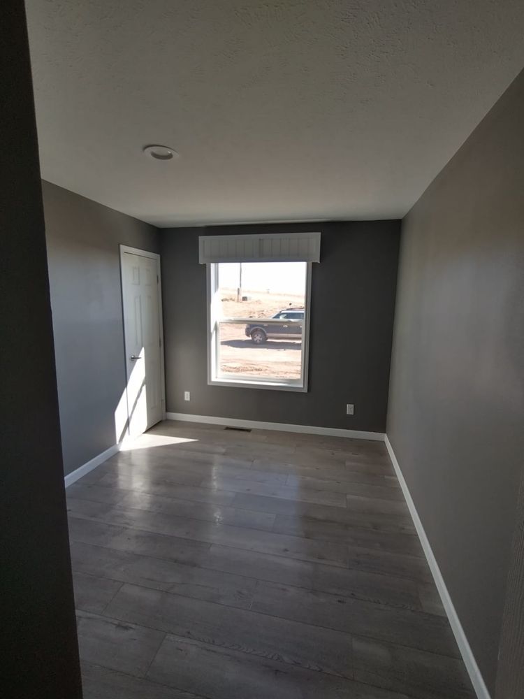 Empty room with gray walls, a window, and a door, with wooden-style flooring.
