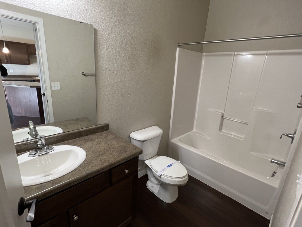 Bathroom with a white tub, toilet, and sink with dark brown cabinets and a mirror.