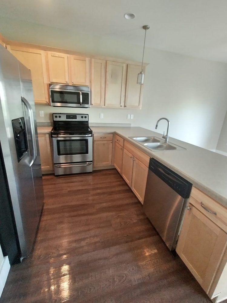 Modern kitchen with stainless steel appliances, light wood cabinets, and gray countertops.