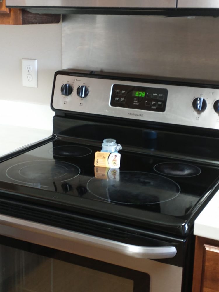 Black electric stove with a timer display. A small item sits on the burner. Stainless steel backsplash.