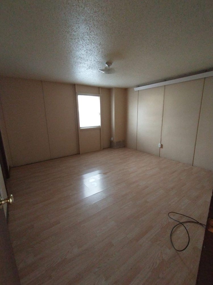 Empty room with light wood-look flooring, light brown walls, and a window.