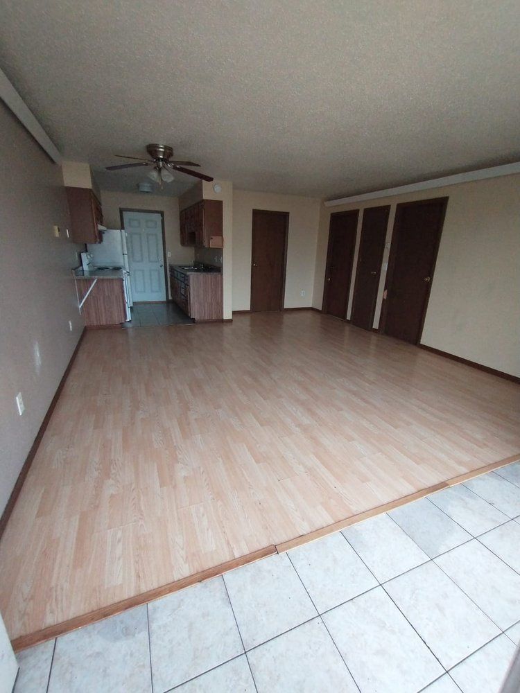 Empty living area with wood flooring, kitchen, and closet doors.