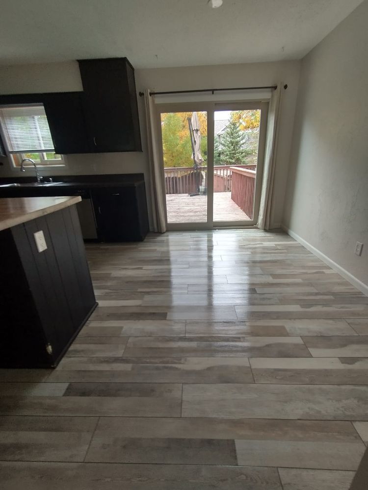 Kitchen with wood-look tile floor, dark cabinets, island, and sliding glass door to a deck with trees.