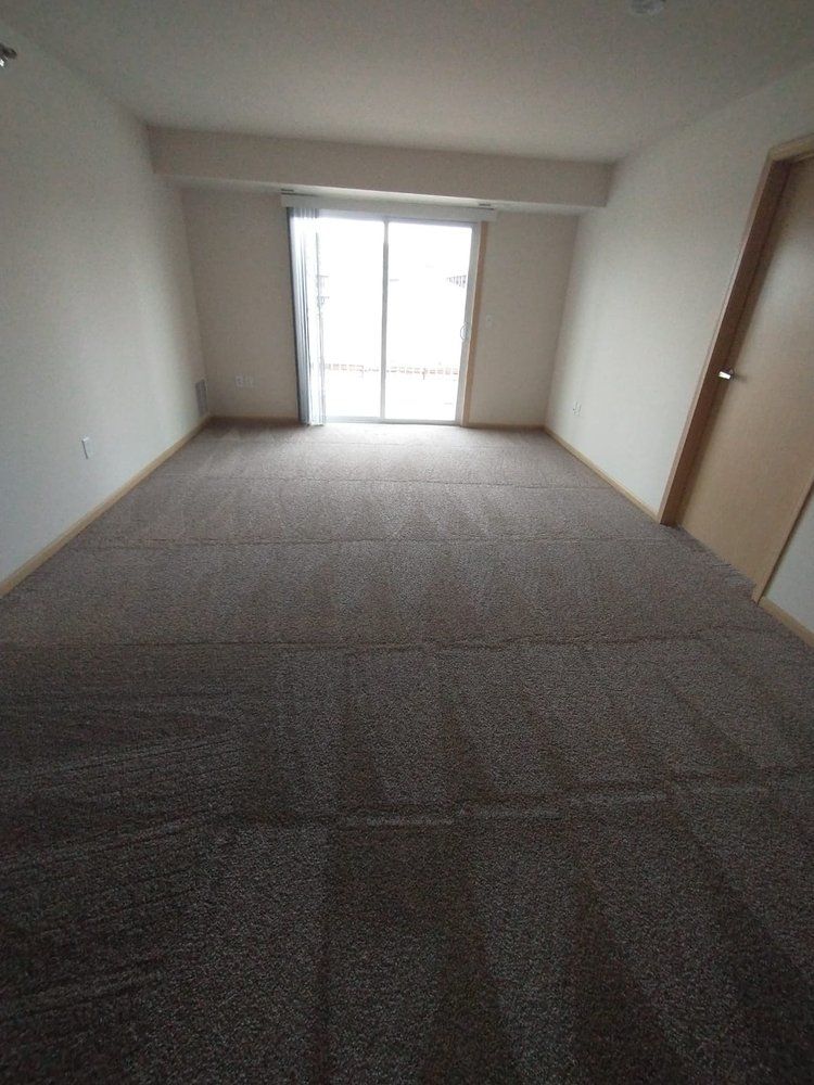 Empty room with brown carpet, sliding glass door, and a closed door.