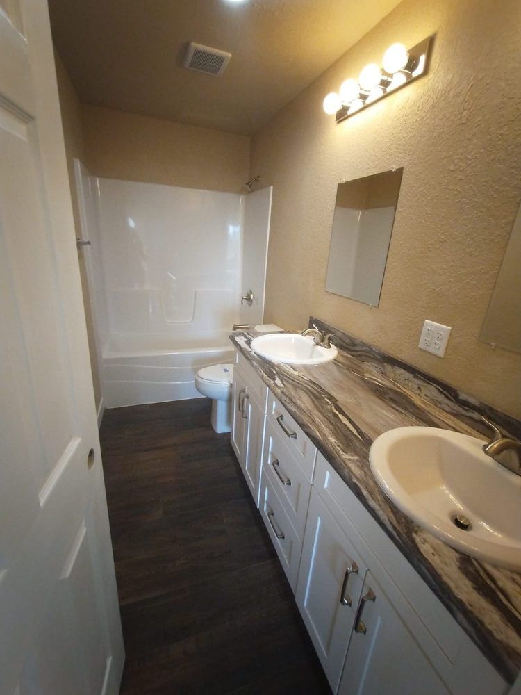 Bathroom with white cabinets, dark countertop, white sink, and tub, dark wood-look floor.