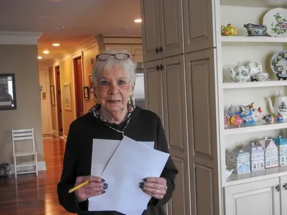 An elderly woman is holding a piece of paper and a pencil in her hands.