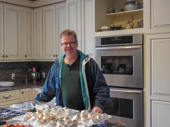 A man is standing in a kitchen holding a tray of food.