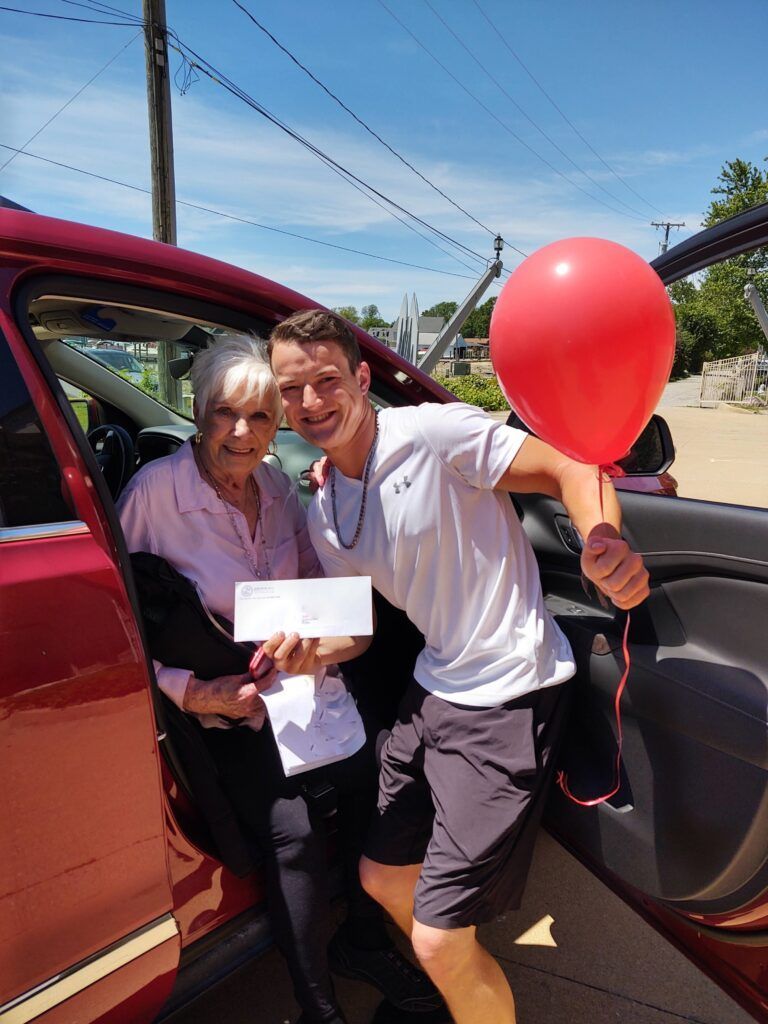A man is holding a red balloon and a check and standing next to a woman.
