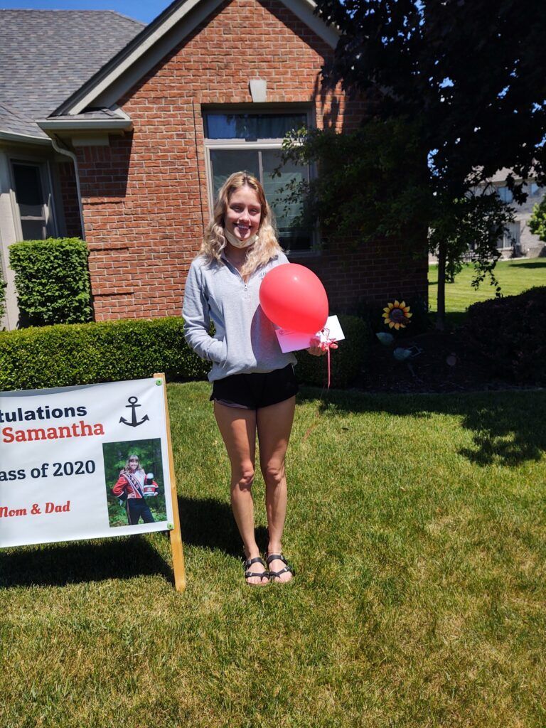 A girl holding a red balloon in front of a sign that says congratulations Samantha.