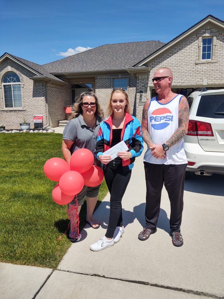 A woman holding a check stands next to her parents.
