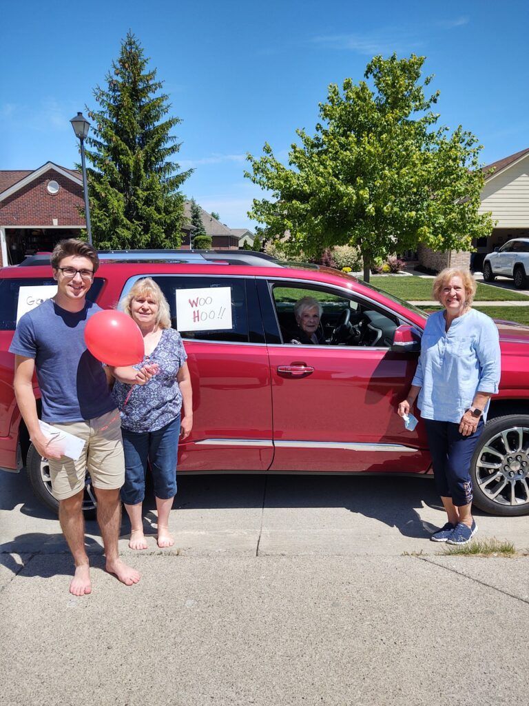 A group of people standing in front of a red SUV that says woo hoo.