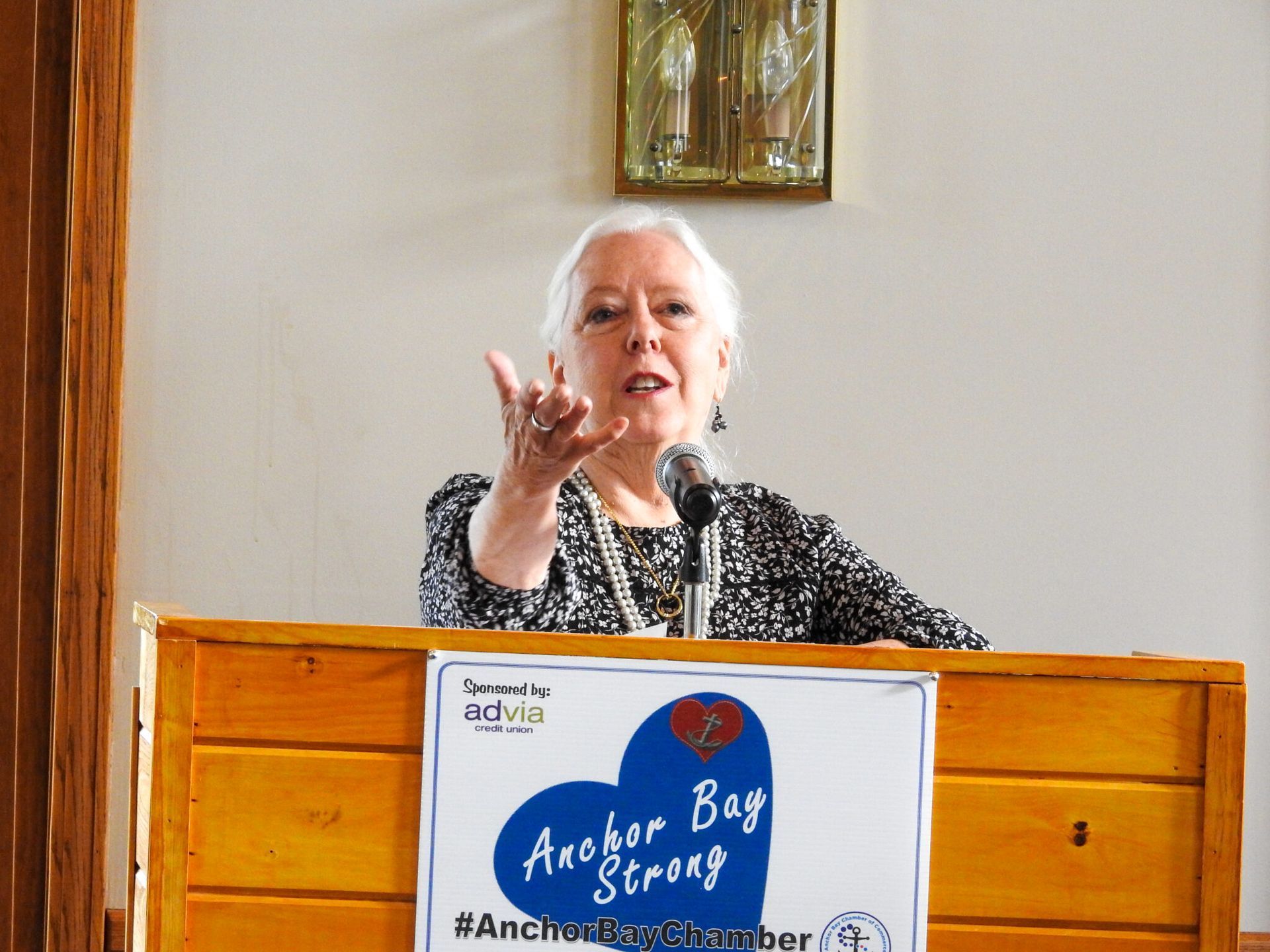 A woman stands at a podium with a sign that says Anchor Bay Strong.