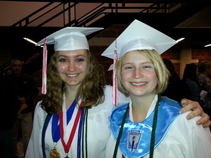 Two girls wearing graduation caps and gowns pose for a picture.