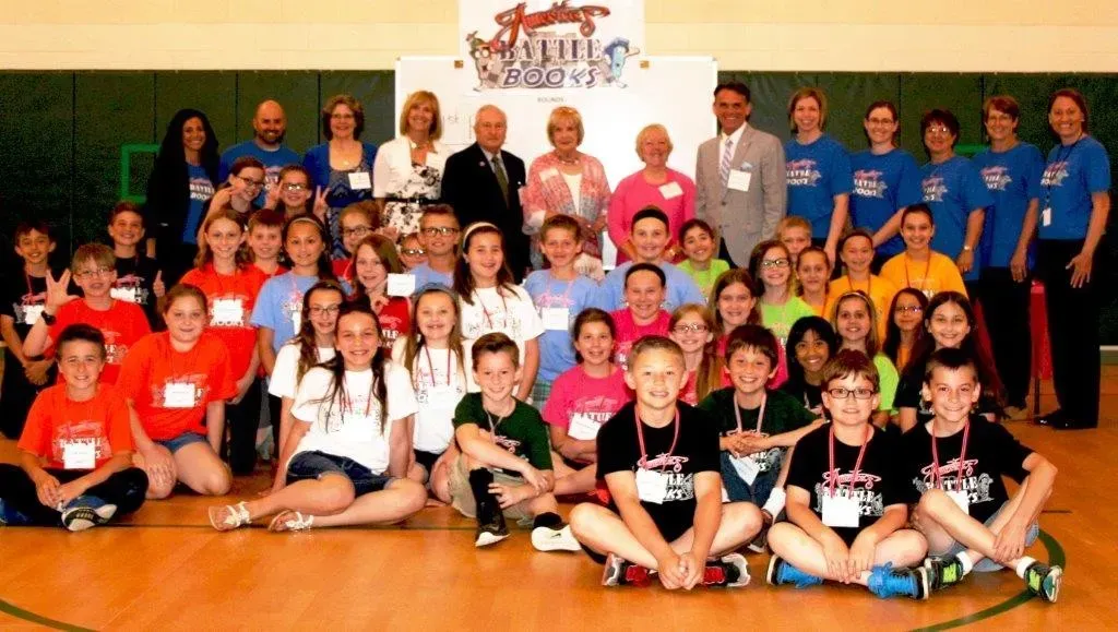 A group of kids and adults in front of a sign reading