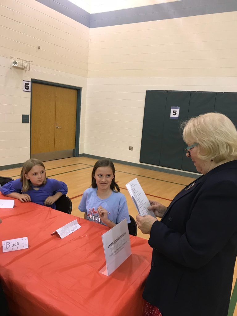 A woman is reading a piece of paper in front of two girls.
