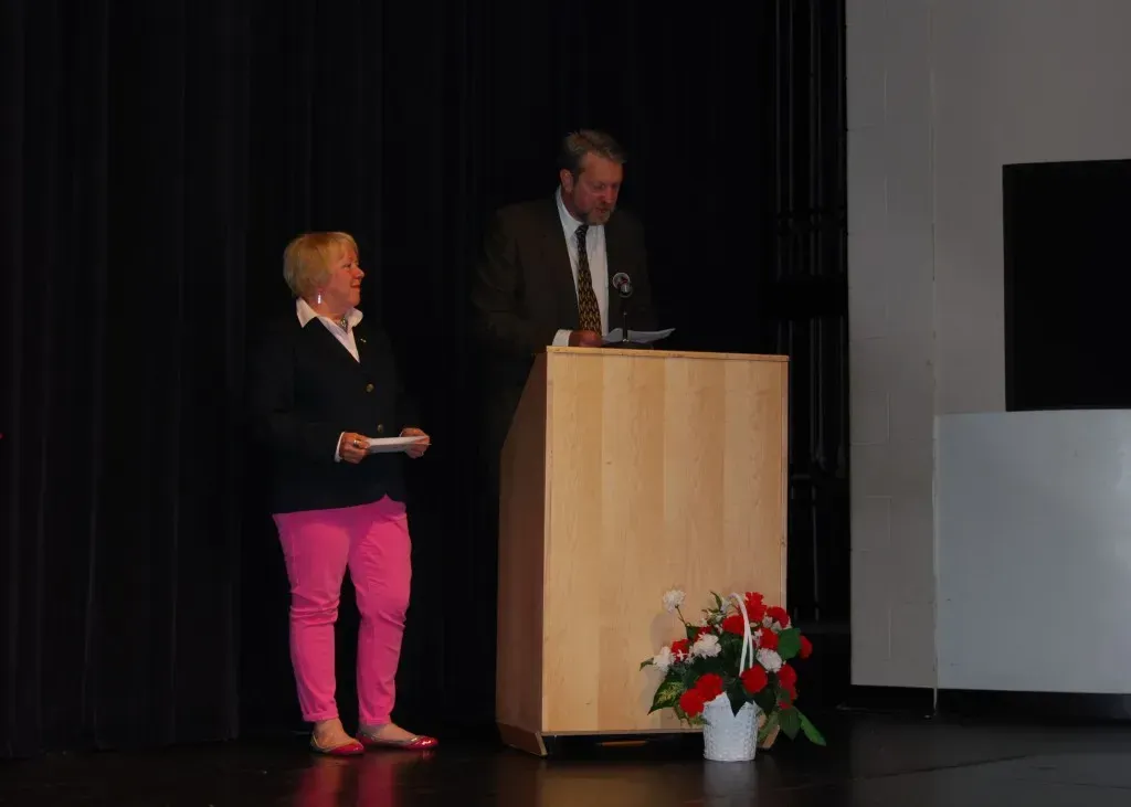 A woman in pink pants stands next to a man at a podium.