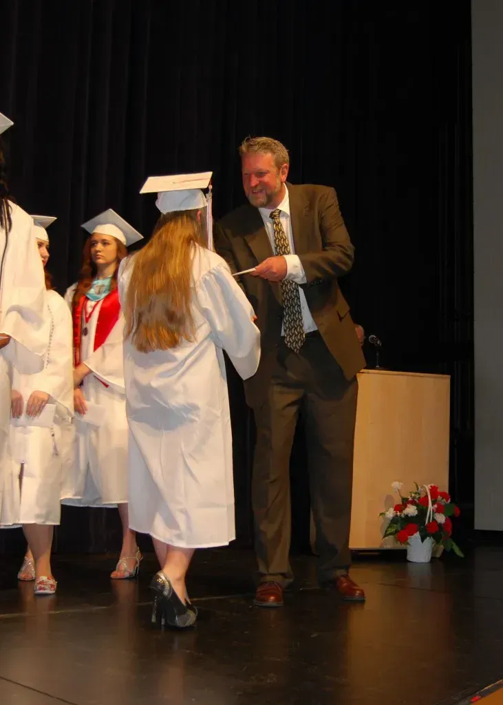 A woman in a white cap and gown is being congratulated by a man in a suit.