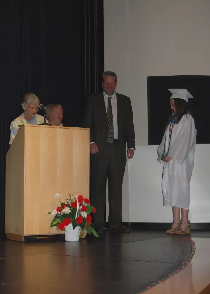 A girl in a graduation cap and gown stands in front of a podium.