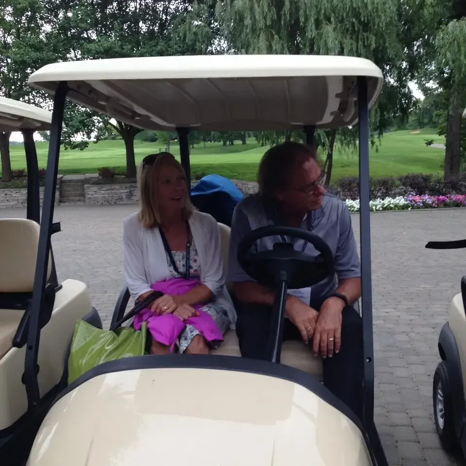 An adult couple sits in a golf cart.